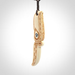 This picture shows a carved hawk in bone. It is a drop shaped pendant. The artist has carved traditional decorative kowhaiwhai designs into the body and these run up the sides of the hawk. These have specific meanings. It is provided with a hand-plaited brown cord that is length adjustable. Shipping is included and we ship worldwide.