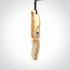 This picture shows a carved hawk in bone. It is a drop shaped pendant. The artist has carved traditional decorative kowhaiwhai designs into the body and these run up the sides of the hawk. These have specific meanings. It is provided with a hand-plaited brown cord that is length adjustable. Shipping is included and we ship worldwide.