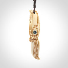 This picture shows a carved hawk in bone. It is a drop shaped pendant. The artist has carved traditional decorative kowhaiwhai designs into the body and these run up the sides of the hawk. These have specific meanings. It is provided with a hand-plaited brown cord that is length adjustable. Shipping is included and we ship worldwide.