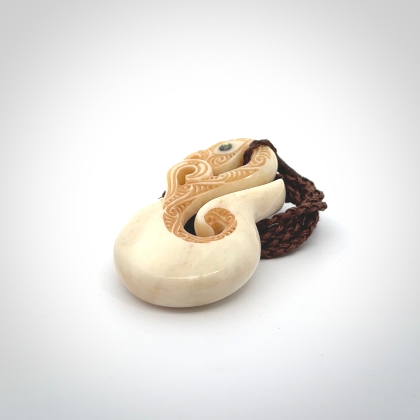 This picture shows a carved manaia in bone. It is provided with a hand-plaited brown cord that is length adjustable.