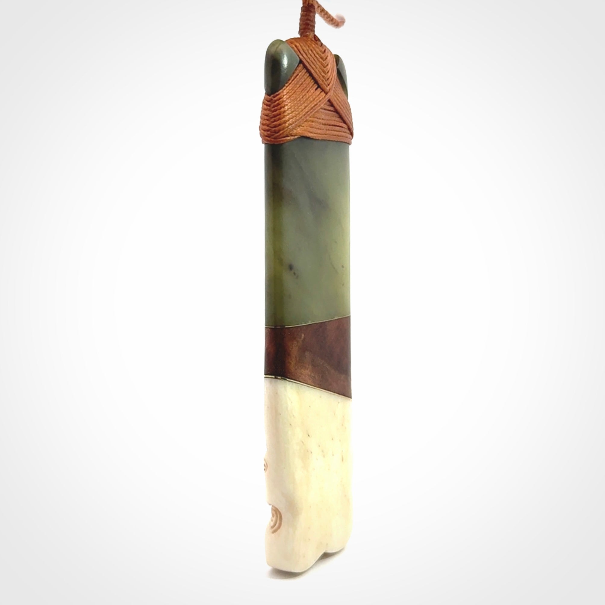 This is a large carved Koruru pendant. It is made from New Zealand Jade, Bone, Kauri wood and Brass. The face of the Koruru is carved with a traditional design in the front. It has a protruding tongue which is also carved and the back face has traditional carved designs. This is a large and very traditional pendant that is a collectors piece.