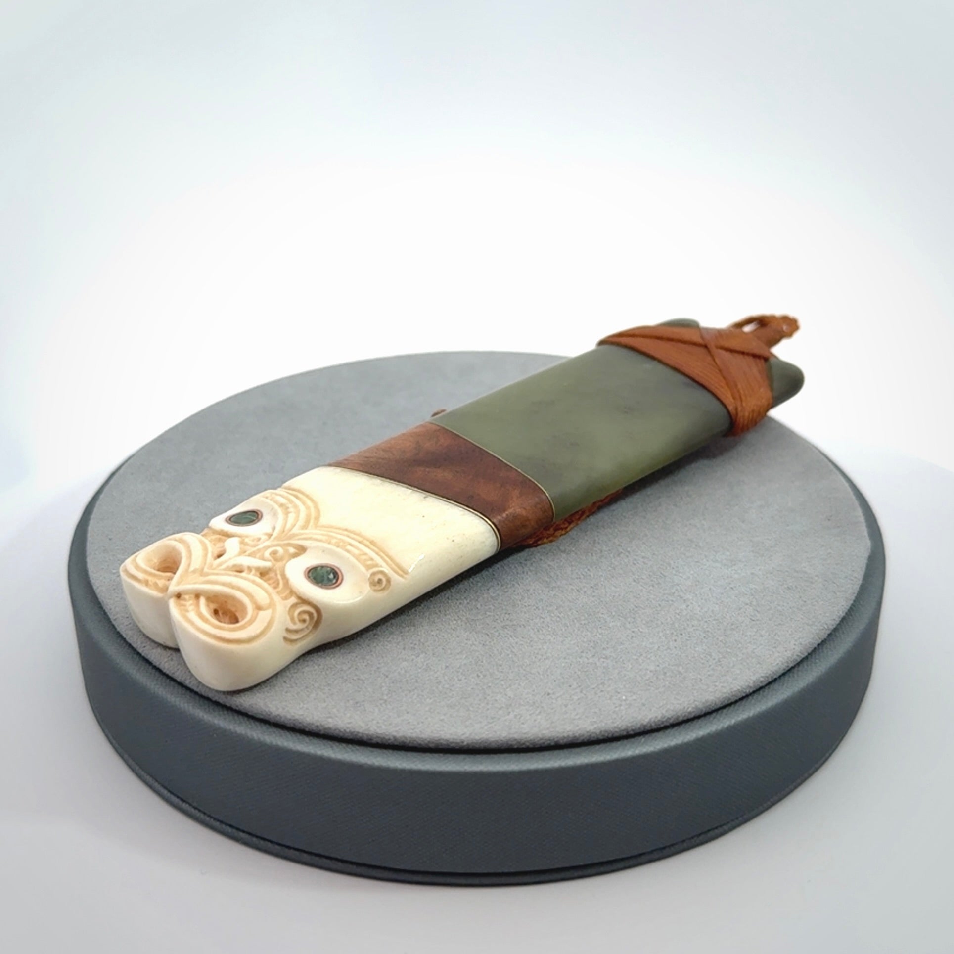 This is a large carved Koruru pendant. It is made from New Zealand Jade, Bone, Kauri wood and Brass. The face of the Koruru is carved with a traditional design in the front. It has a protruding tongue which is also carved and the back face has traditional carved designs. This is a large and very traditional pendant that is a collectors piece.