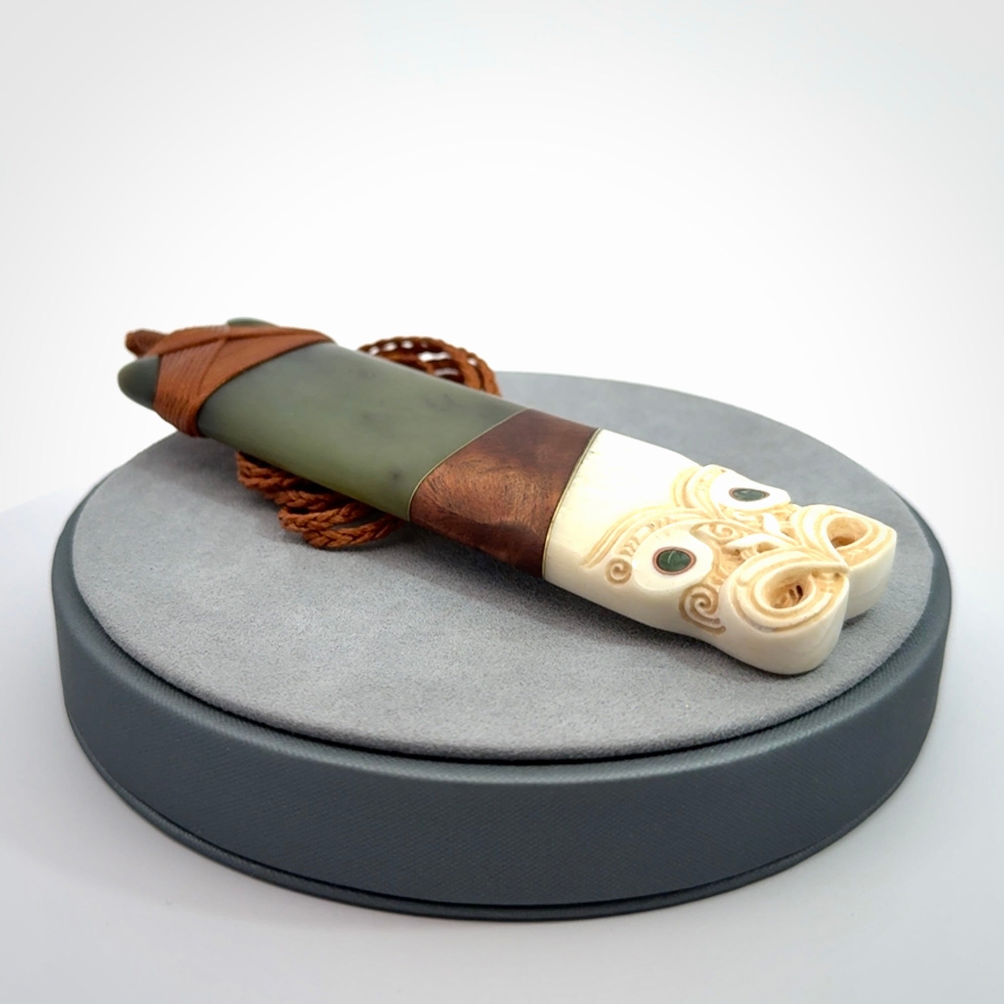 This is a large carved Koruru pendant. It is made from New Zealand Jade, Bone, Kauri wood and Brass. The face of the Koruru is carved with a traditional design in the front. It has a protruding tongue which is also carved and the back face has traditional carved designs. This is a large and very traditional pendant that is a collectors piece.