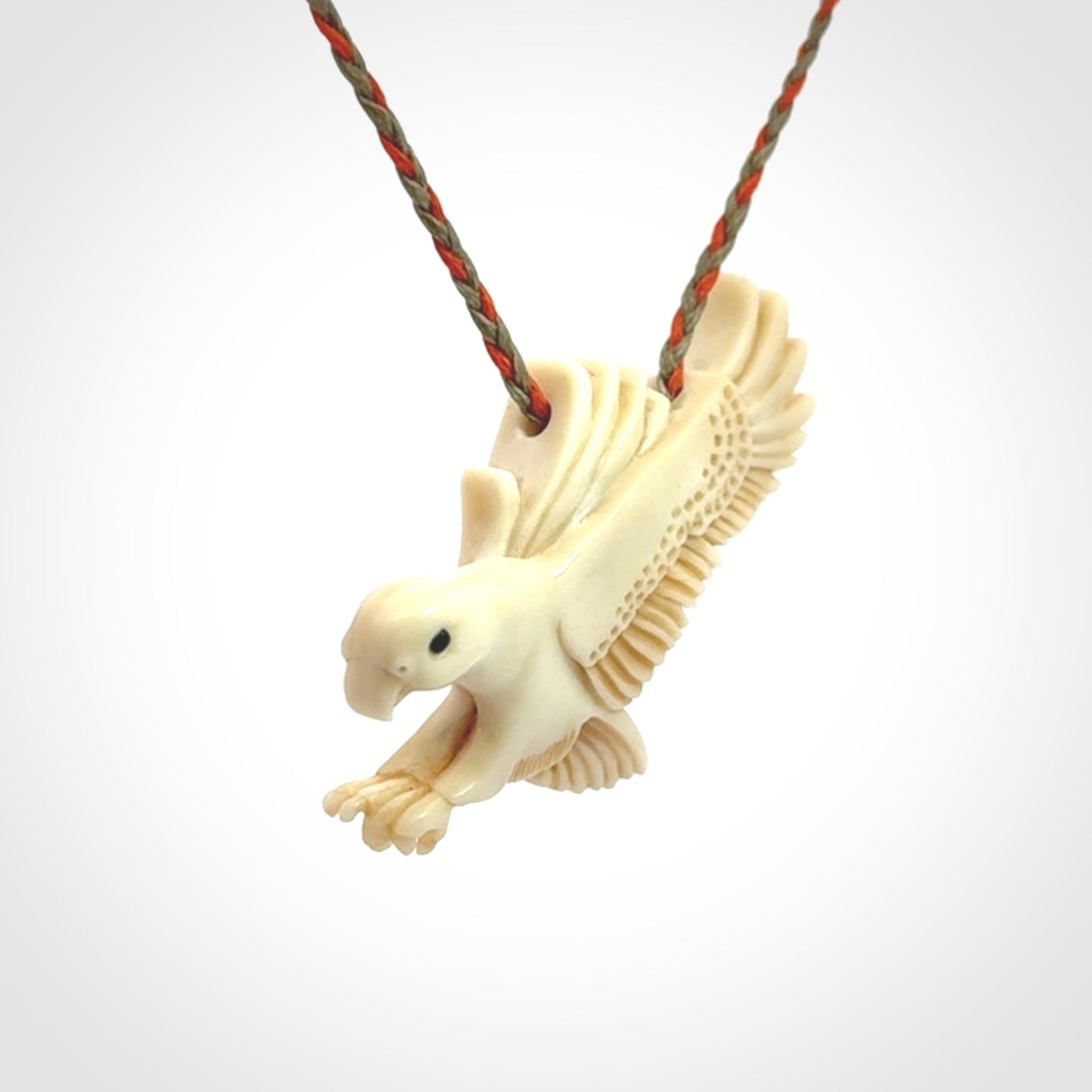 This picture shows a carved kea pendant in bone. It is provided with a hand-plaited orange and olive cord that is length adjustable. Shipping is included and we ship worldwide.