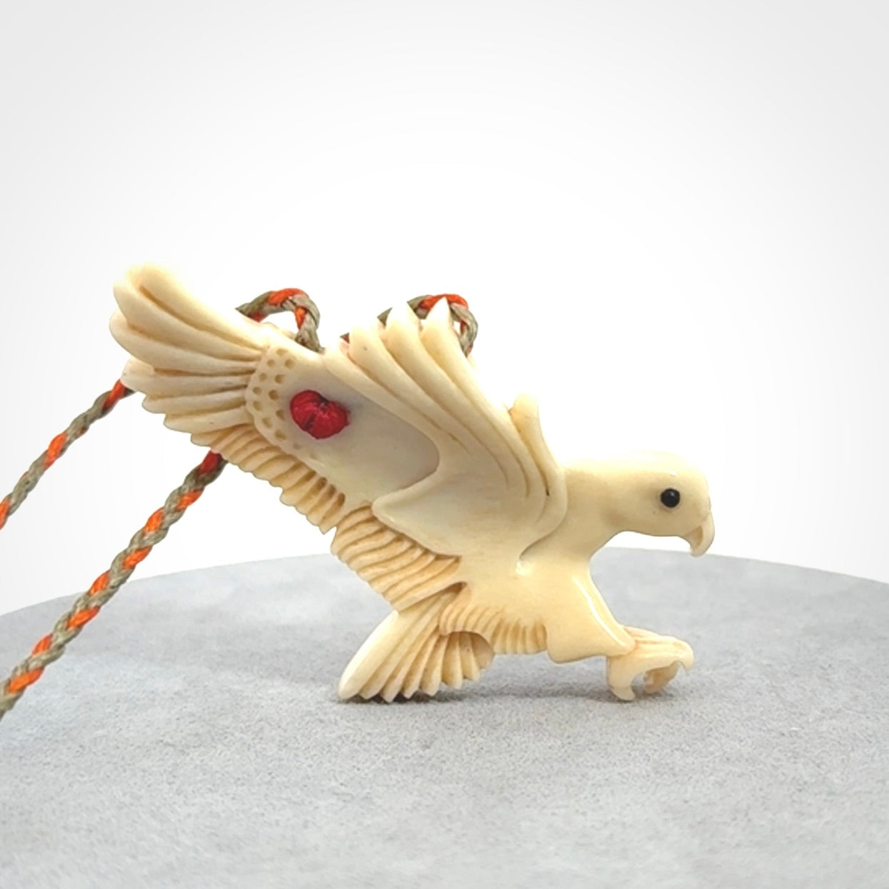 This picture shows a carved kea pendant in bone. It is provided with a hand-plaited orange and olive cord that is length adjustable. Shipping is included and we ship worldwide.