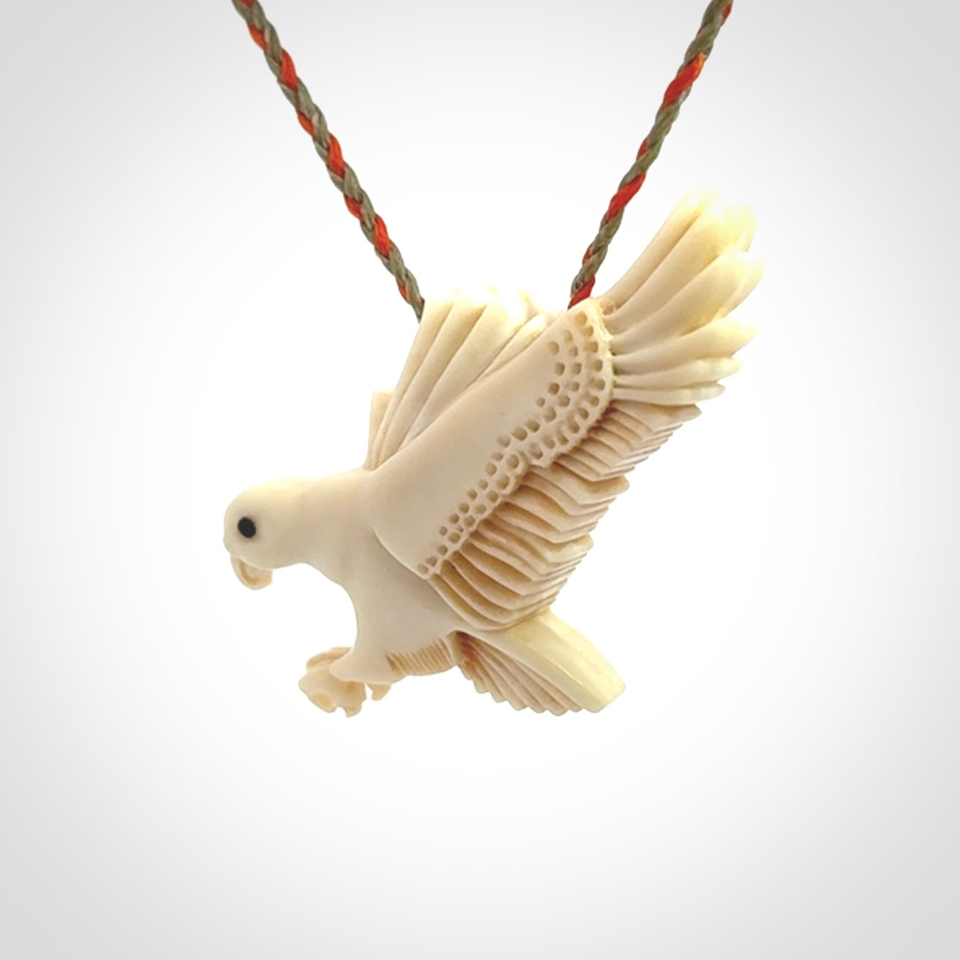 This picture shows a carved kea pendant in bone. It is provided with a hand-plaited orange and olive cord that is length adjustable. Shipping is included and we ship worldwide.