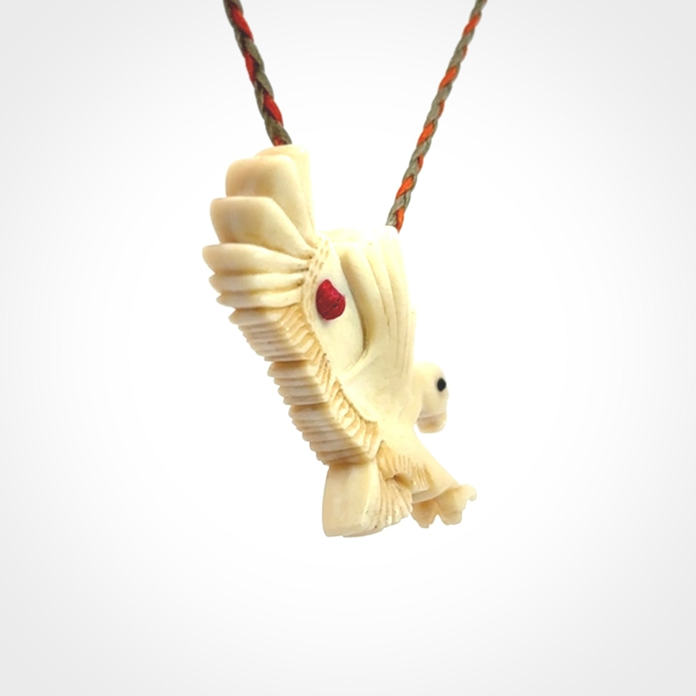 This picture shows a carved kea pendant in bone. It is provided with a hand-plaited orange and olive cord that is length adjustable. Shipping is included and we ship worldwide.