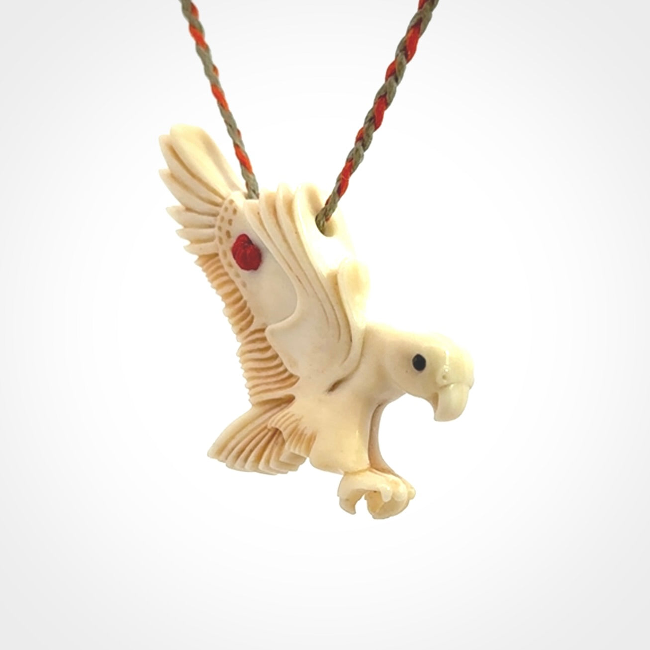 This picture shows a carved kea pendant in bone. It is provided with a hand-plaited orange and olive cord that is length adjustable. Shipping is included and we ship worldwide.