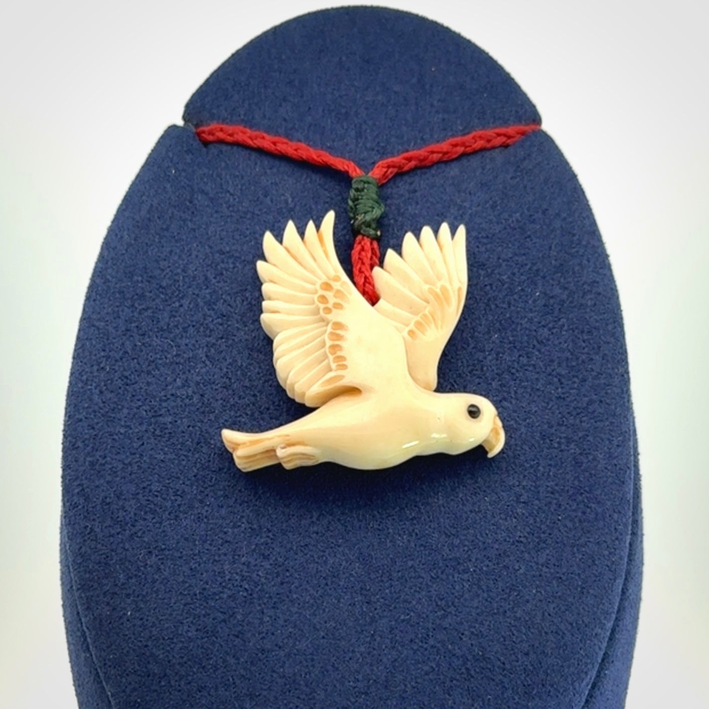 This picture shows a carved kea pendant in bone. It is provided with a hand-plaited red cord that is length adjustable. Shipping is included and we ship worldwide.