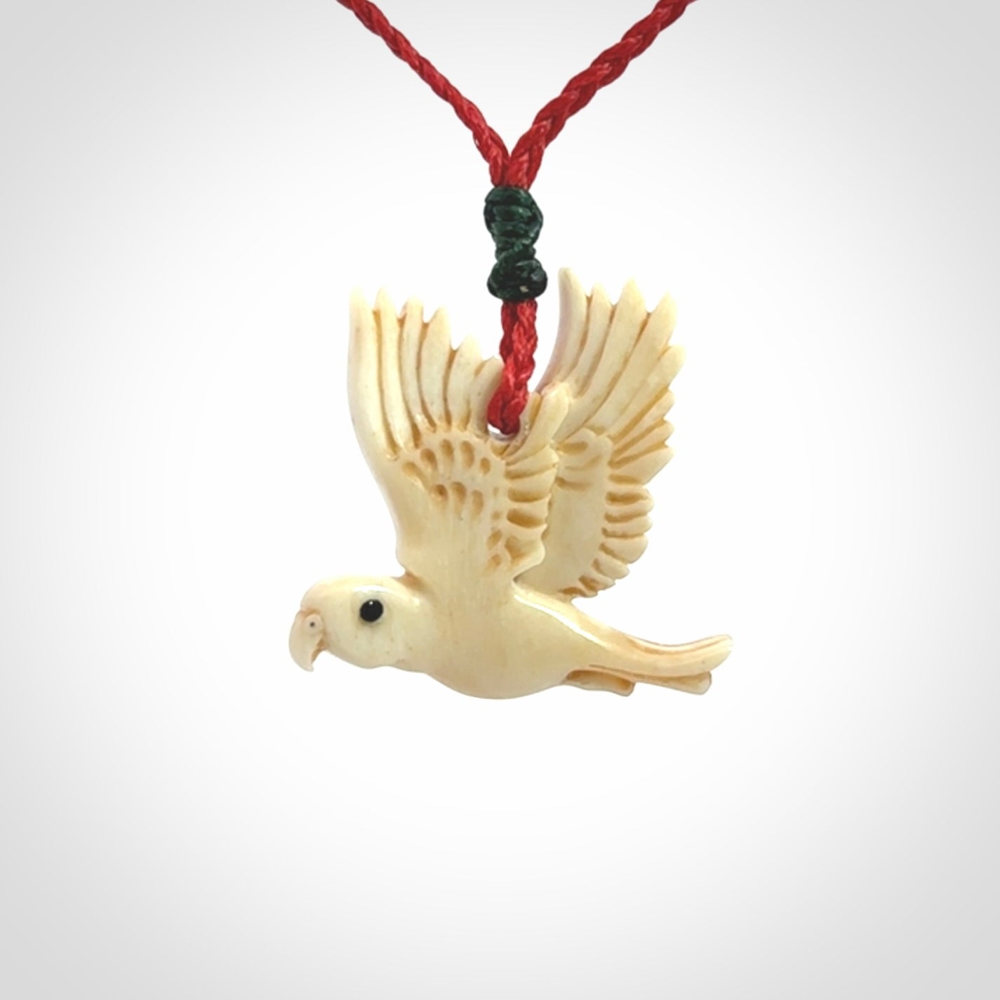 This picture shows a carved kea pendant in bone. It is provided with a hand-plaited red cord that is length adjustable. Shipping is included and we ship worldwide.