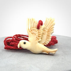 This picture shows a carved kea pendant in bone. It is provided with a hand-plaited red cord that is length adjustable. Shipping is included and we ship worldwide.