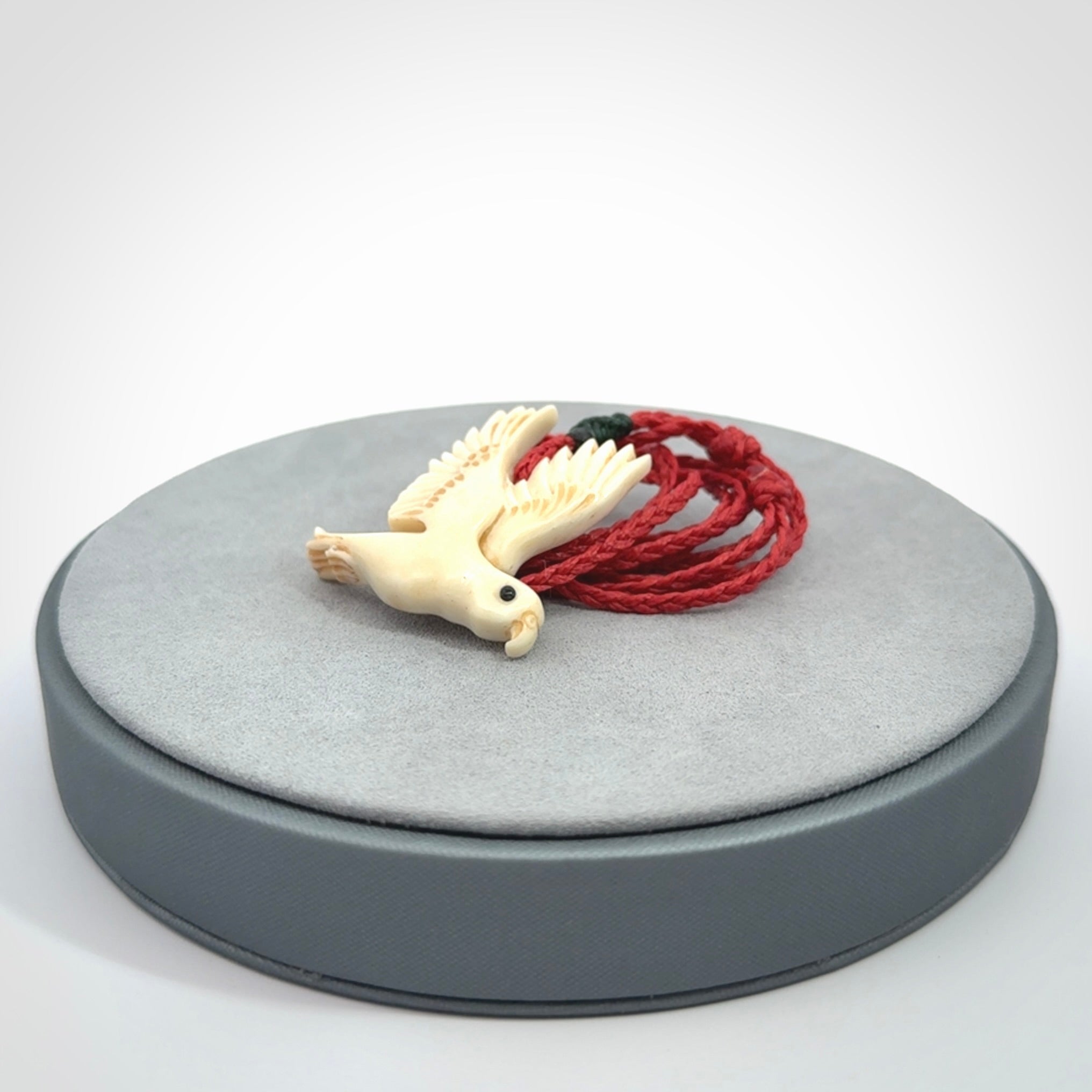 This picture shows a carved kea pendant in bone. It is provided with a hand-plaited red cord that is length adjustable. Shipping is included and we ship worldwide.