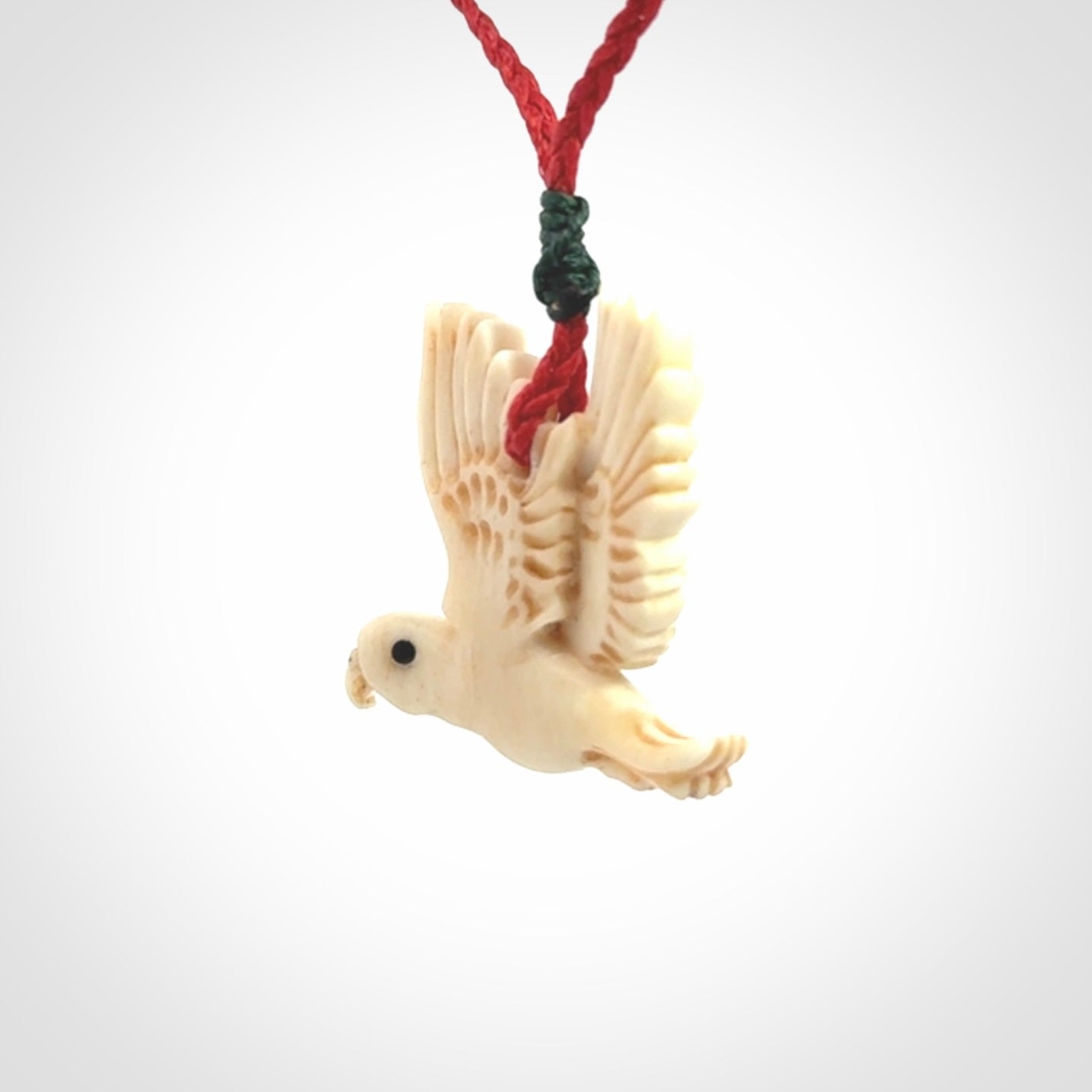 This picture shows a carved kea pendant in bone. It is provided with a hand-plaited red cord that is length adjustable. Shipping is included and we ship worldwide.