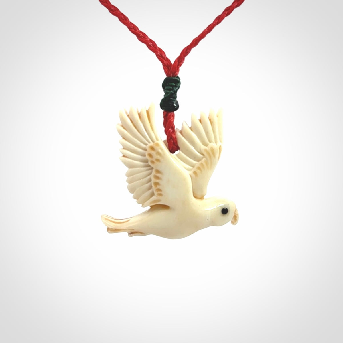 This picture shows a carved kea pendant in bone. It is provided with a hand-plaited red cord that is length adjustable. Shipping is included and we ship worldwide.