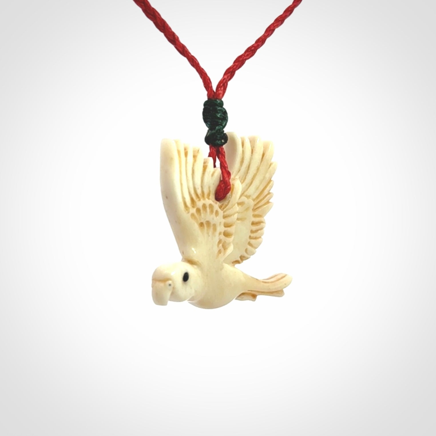 This picture shows a carved kea pendant in bone. It is provided with a hand-plaited red cord that is length adjustable. Shipping is included and we ship worldwide.