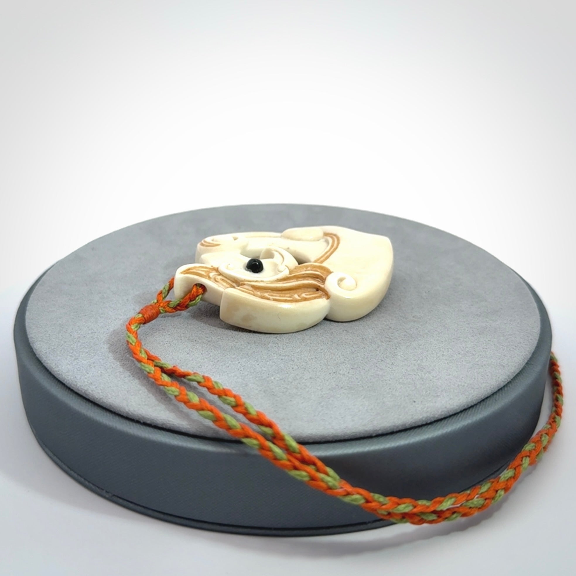 This picture shows a carved kea pendant in bone. It is provided with a hand-plaited orange and green cord that is length adjustable. Shipping is included and we ship worldwide.