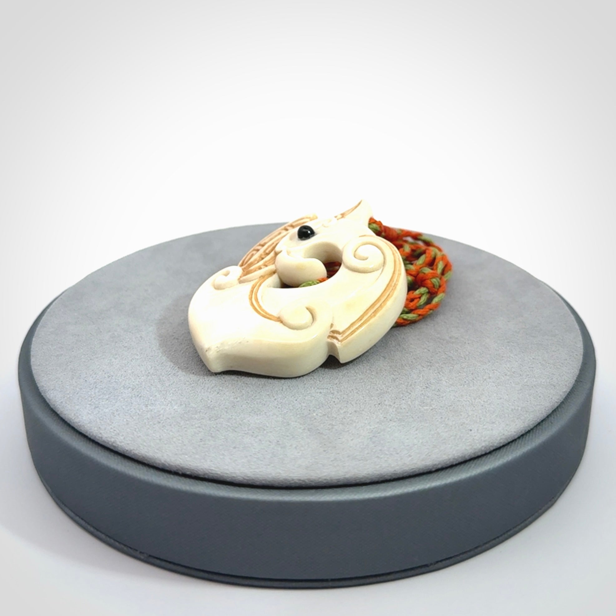 This picture shows a carved kea pendant in bone. It is provided with a hand-plaited orange and green cord that is length adjustable. Shipping is included and we ship worldwide.
