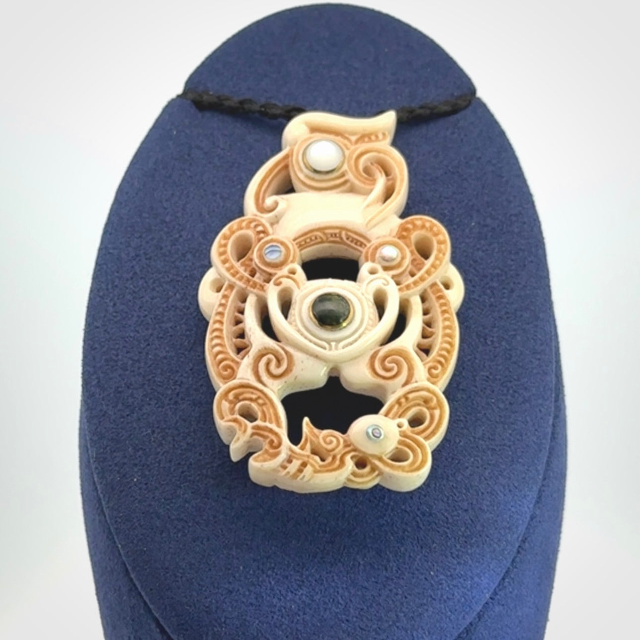 Hand carved bone manaia pendant with Jade, Mother of Pearl, Paua shell and Brass inlay. This is a complex carving by New Zealand carver and artist, Andrew Doughty. It is an intricate representation of a manaia carved to represent protection. It can be worn but is also a quality that warrants display.