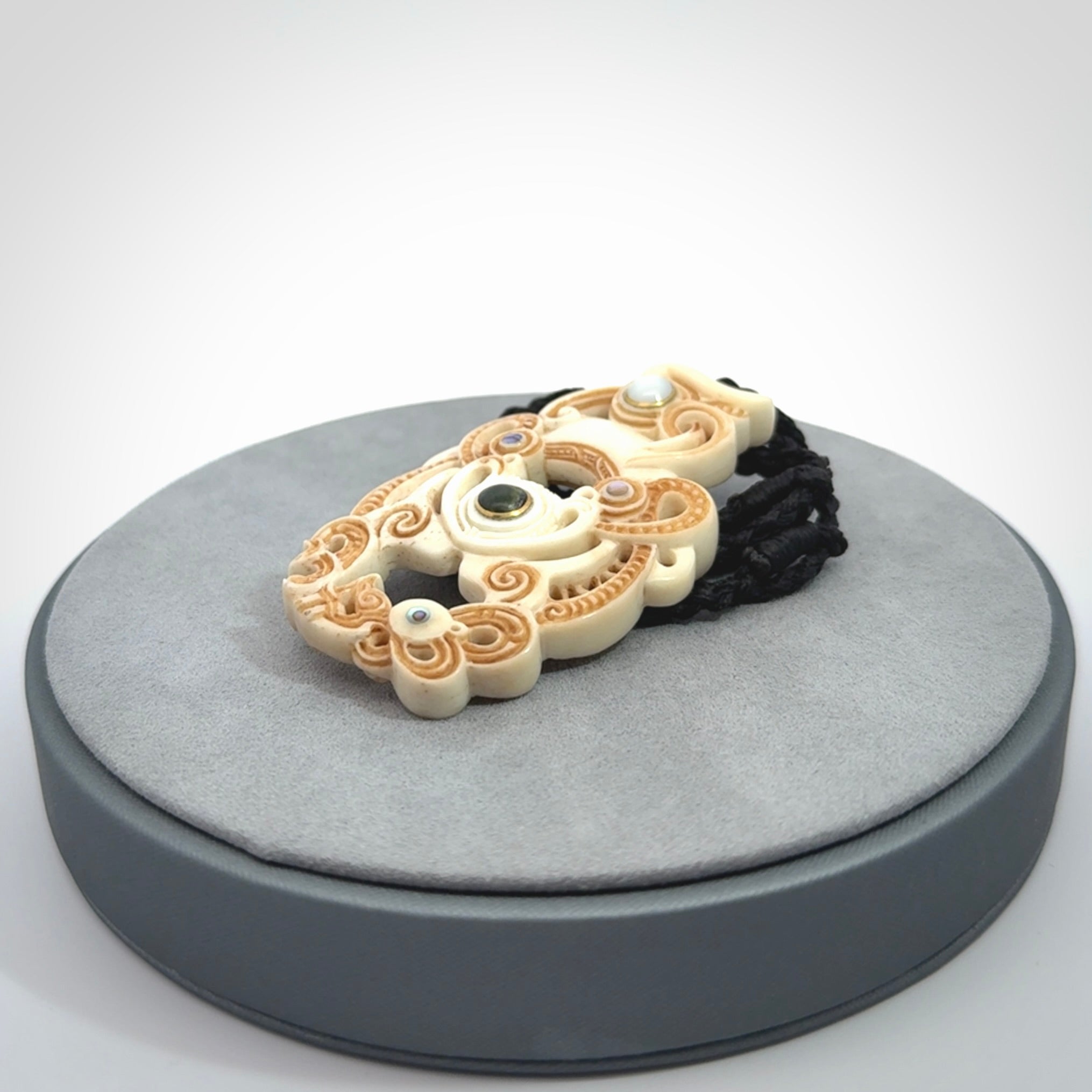 Hand carved bone manaia pendant with Jade, Mother of Pearl, Paua shell and Brass inlay. This is a complex carving by New Zealand carver and artist, Andrew Doughty. It is an intricate representation of a manaia carved to represent protection. It can be worn but is also a quality that warrants display.