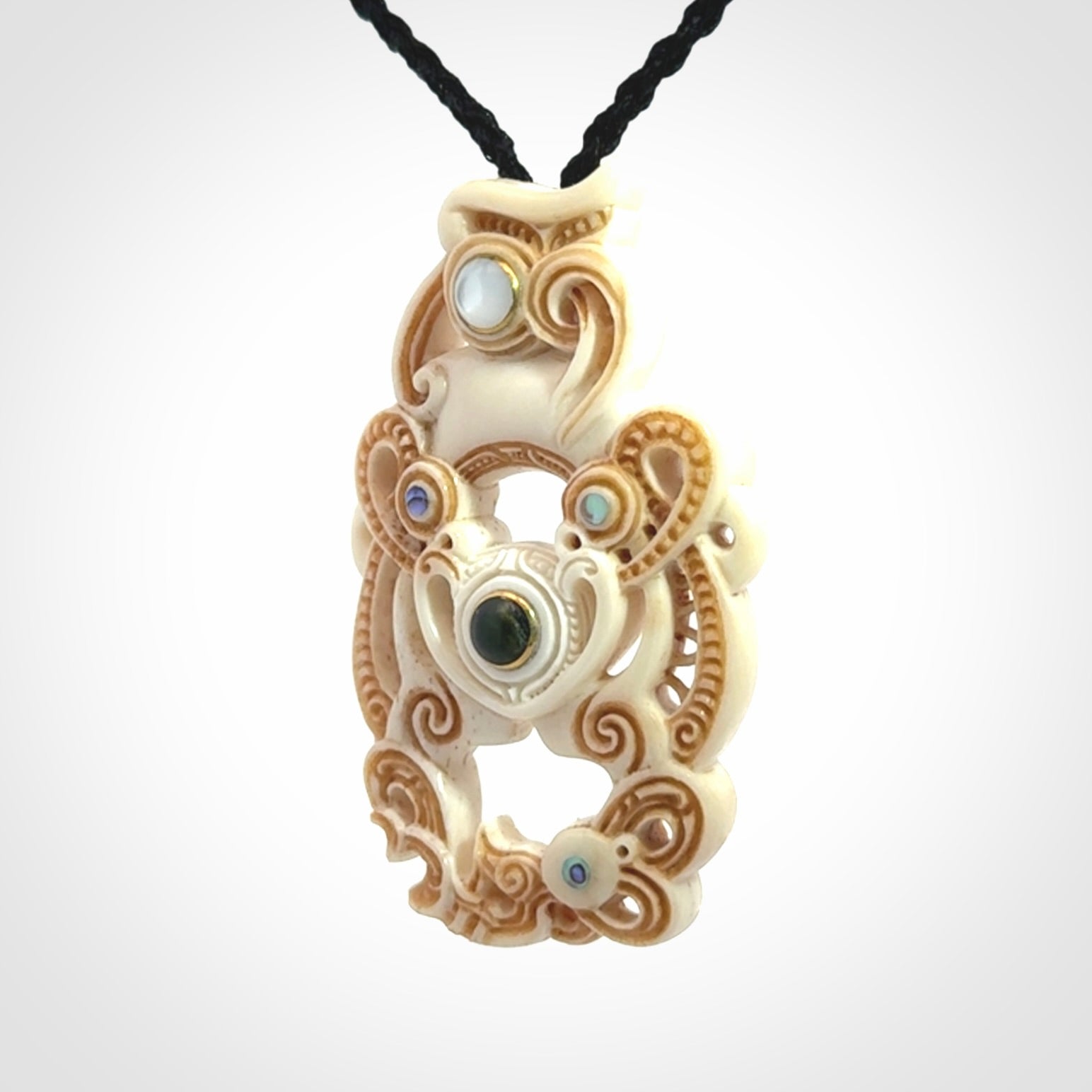 Hand carved bone manaia pendant with Jade, Mother of Pearl, Paua shell and Brass inlay. This is a complex carving by New Zealand carver and artist, Andrew Doughty. It is an intricate representation of a manaia carved to represent protection. It can be worn but is also a quality that warrants display.