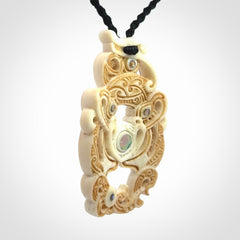 Hand carved bone manaia pendant with Jade, Mother of Pearl, Paua shell and Brass inlay. This is a complex carving by New Zealand carver and artist, Andrew Doughty. It is an intricate representation of a manaia carved to represent protection. It can be worn but is also a quality that warrants display.