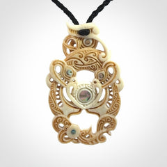 Hand carved bone manaia pendant with Jade, Mother of Pearl, Paua shell and Brass inlay. This is a complex carving by New Zealand carver and artist, Andrew Doughty. It is an intricate representation of a manaia carved to represent protection. It can be worn but is also a quality that warrants display.