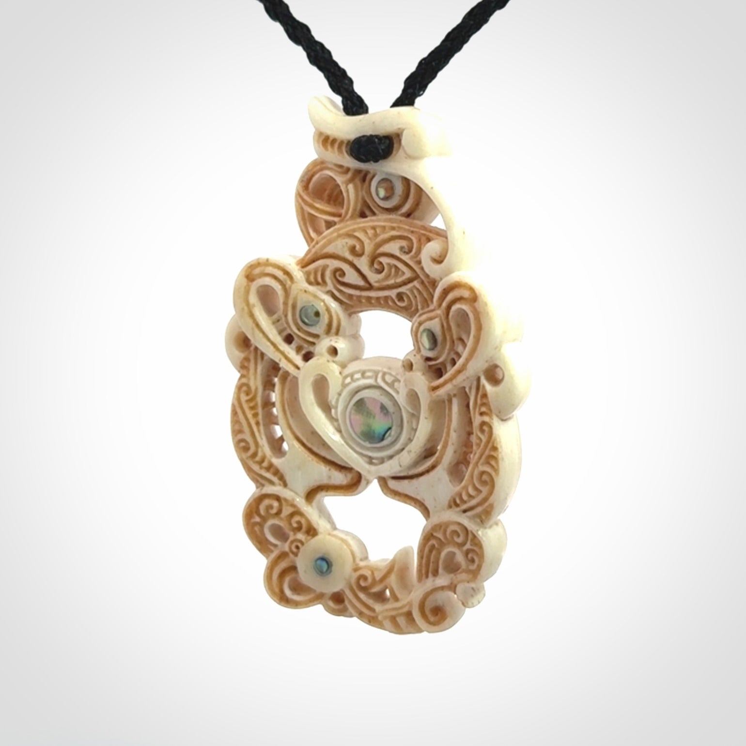Hand carved bone manaia pendant with Jade, Mother of Pearl, Paua shell and Brass inlay. This is a complex carving by New Zealand carver and artist, Andrew Doughty. It is an intricate representation of a manaia carved to represent protection. It can be worn but is also a quality that warrants display.