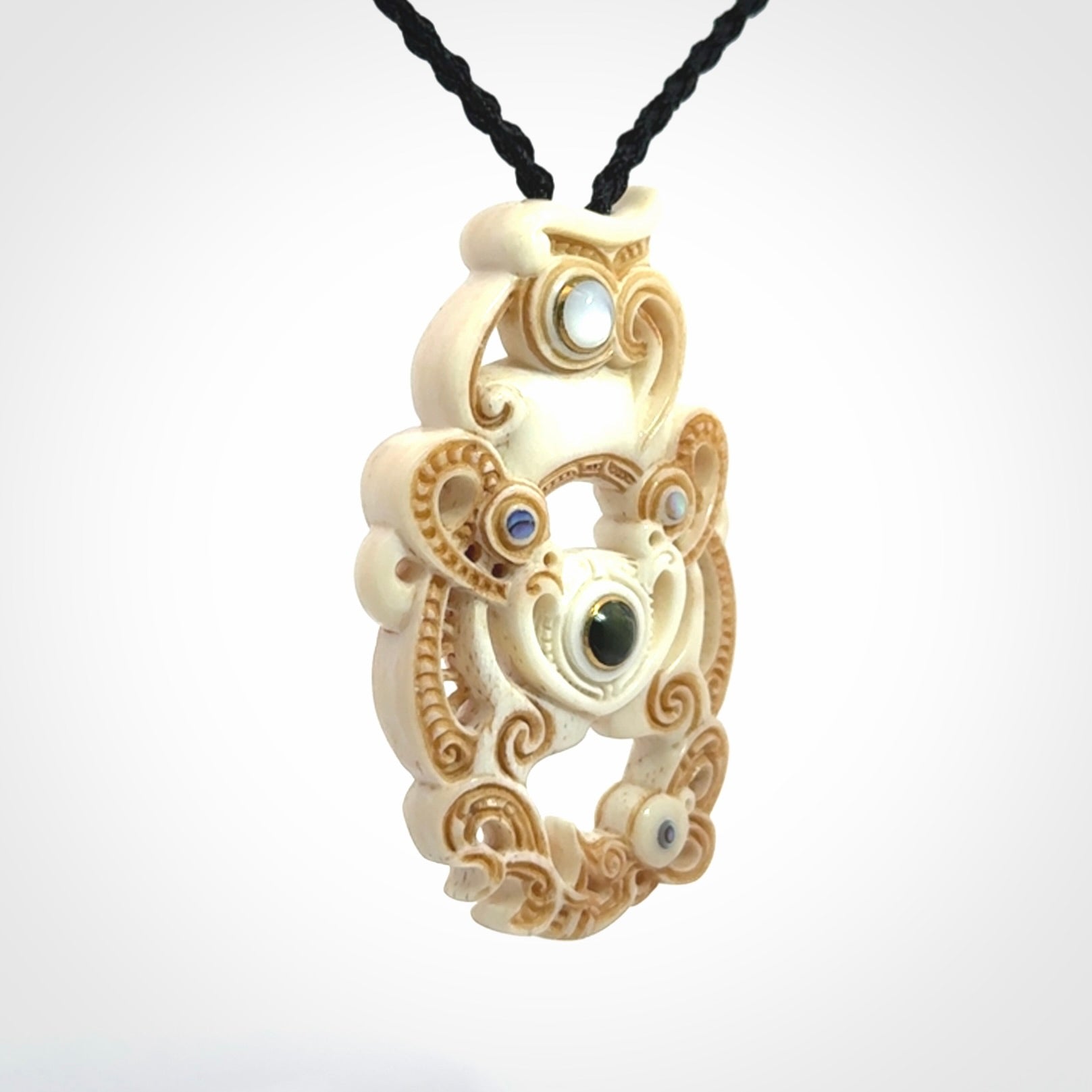 Hand carved bone manaia pendant with Jade, Mother of Pearl, Paua shell and Brass inlay. This is a complex carving by New Zealand carver and artist, Andrew Doughty. It is an intricate representation of a manaia carved to represent protection. It can be worn but is also a quality that warrants display.