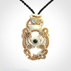Hand carved bone manaia pendant with Jade, Mother of Pearl, Paua shell and Brass inlay. This is a complex carving by New Zealand carver and artist, Andrew Doughty. It is an intricate representation of a manaia carved to represent protection. It can be worn but is also a quality that warrants display.