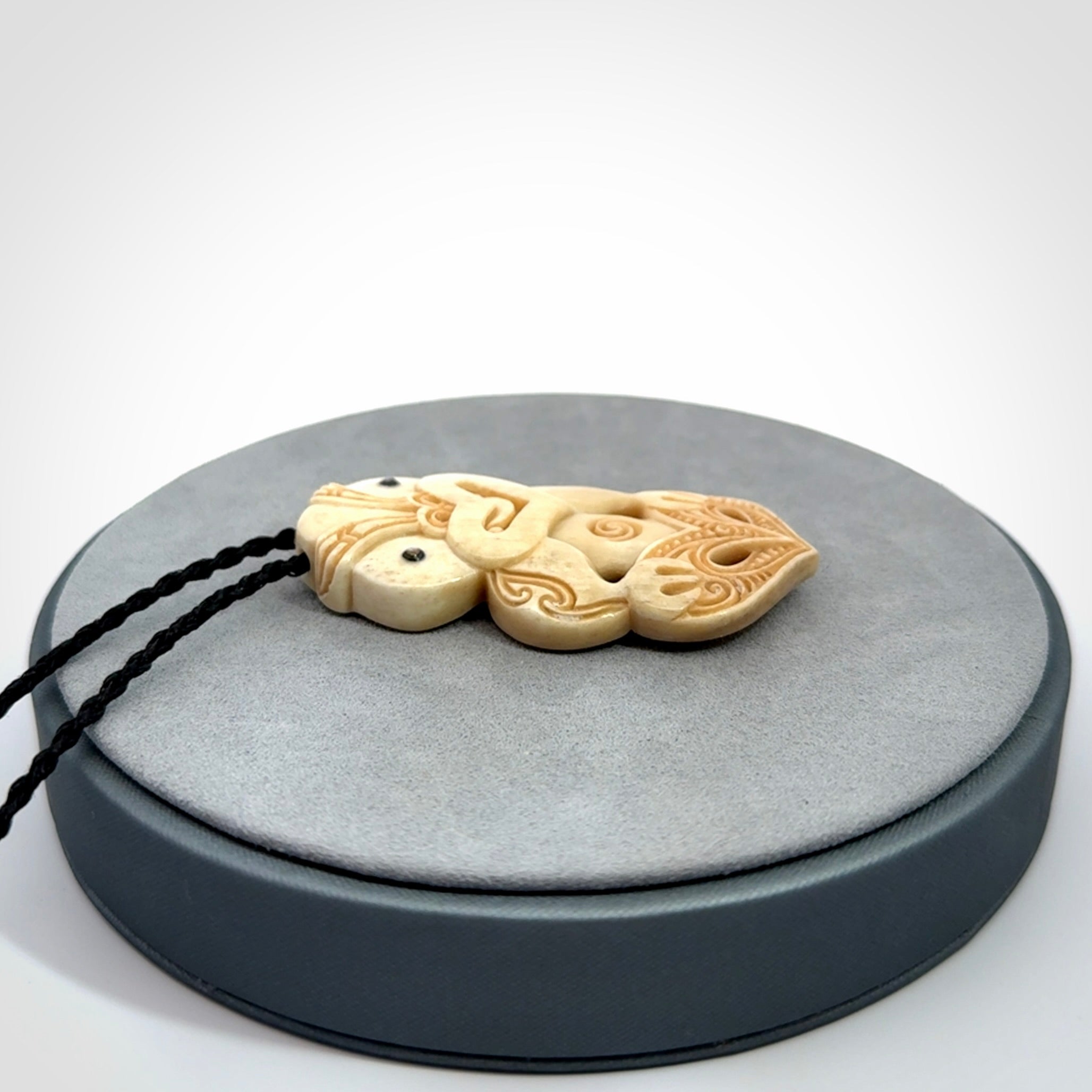 This picture shows a carved Tiki pendant in bone. It is provided with a hand-plaited black cord that is length adjustable.