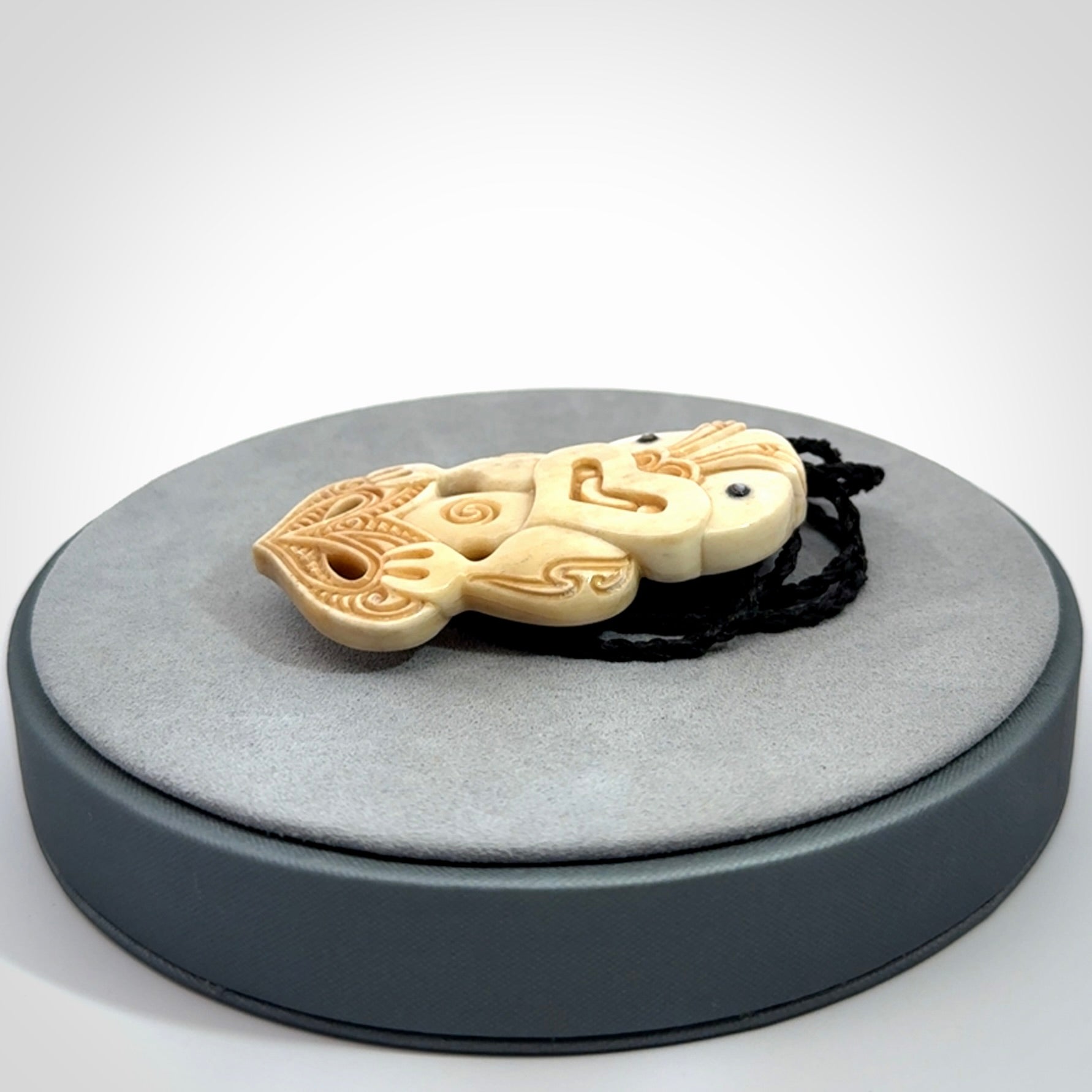 This picture shows a carved Tiki pendant in bone. It is provided with a hand-plaited black cord that is length adjustable.