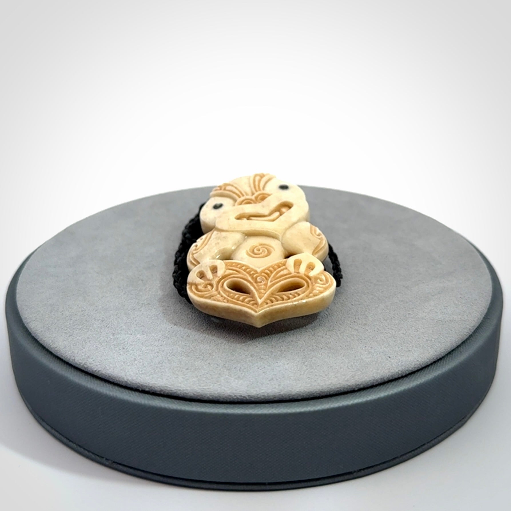 This picture shows a carved Tiki pendant in bone. It is provided with a hand-plaited black cord that is length adjustable.