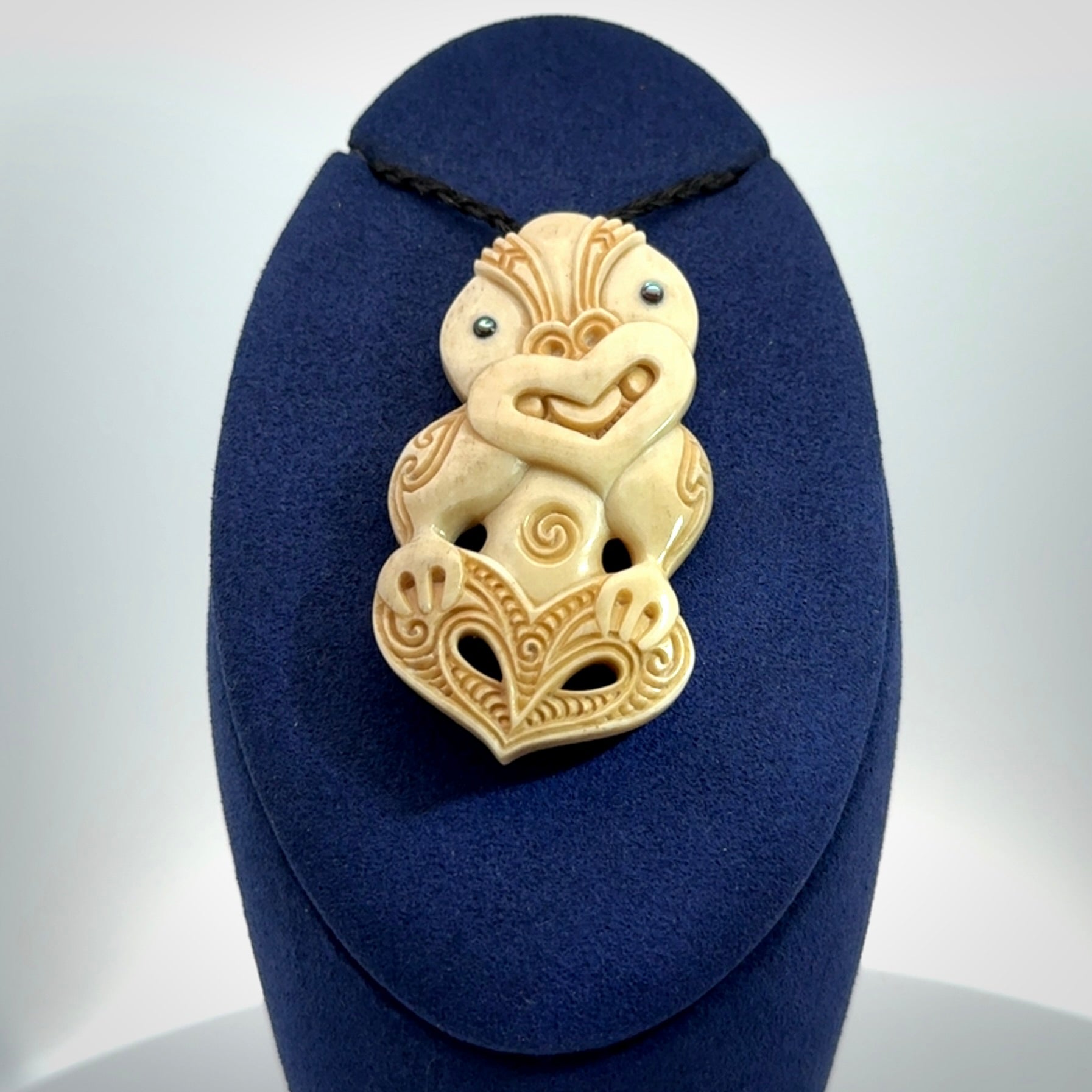 This picture shows a carved Tiki pendant in bone. It is provided with a hand-plaited black cord that is length adjustable.