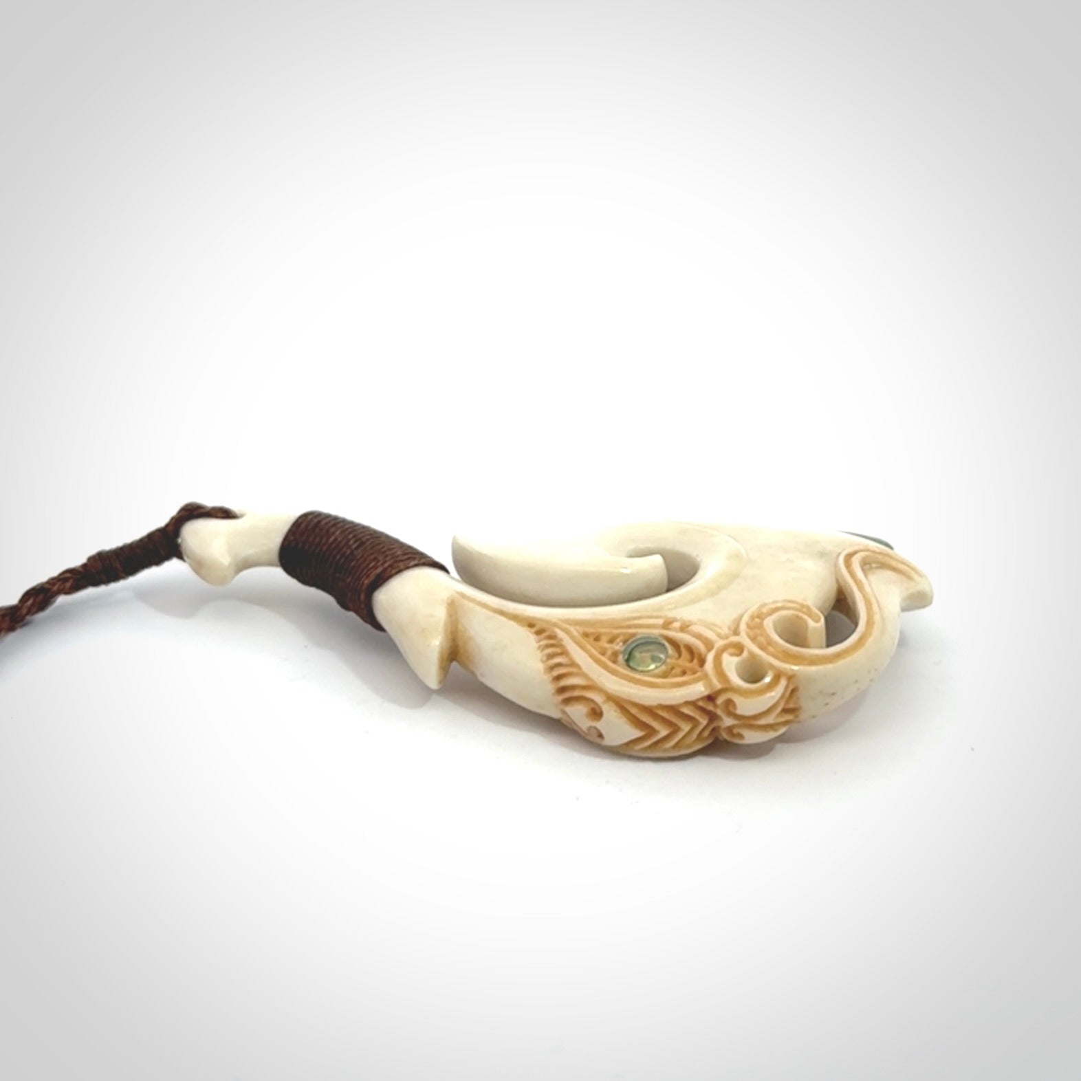 This picture shows a carved manaia matau in bone with Jade and Paua shell. It is provided with a hand-plaited brown cord that is length adjustable. Free shipping worldwide.