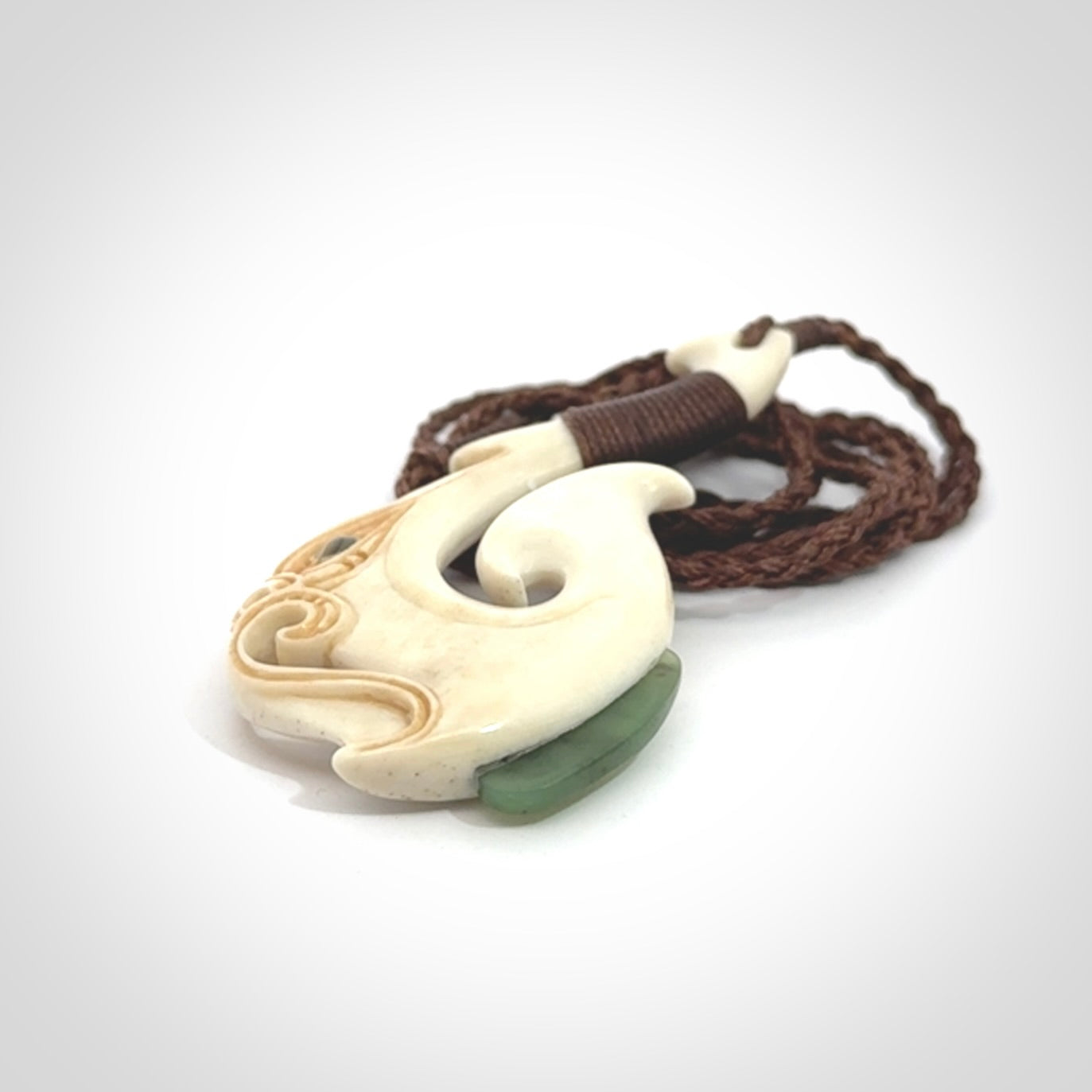 This picture shows a carved manaia matau in bone with Jade and Paua shell. It is provided with a hand-plaited brown cord that is length adjustable. Free shipping worldwide.