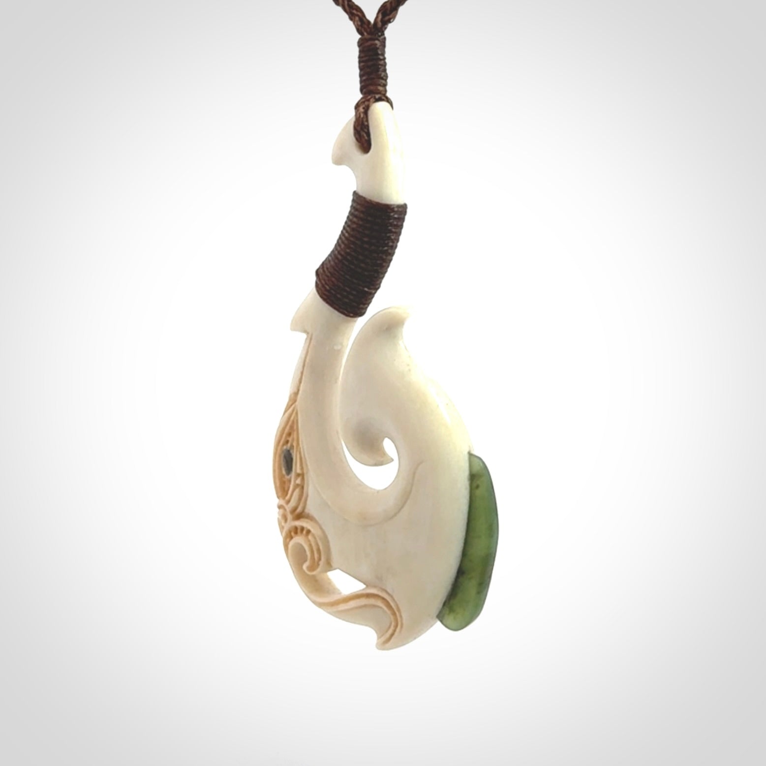 This picture shows a carved manaia matau in bone with Jade and Paua shell. It is provided with a hand-plaited brown cord that is length adjustable. Free shipping worldwide.