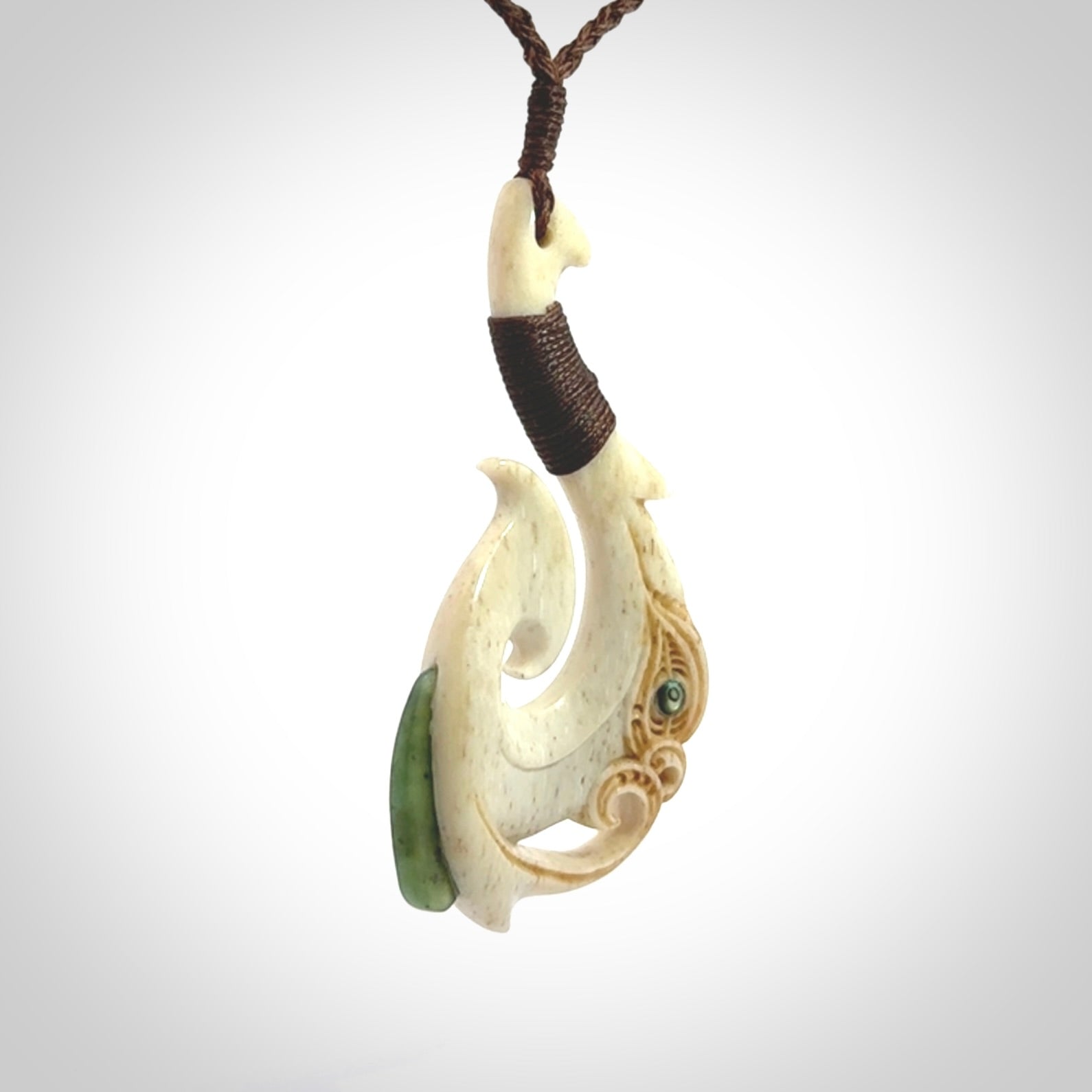 This picture shows a carved manaia matau in bone with Jade and Paua shell. It is provided with a hand-plaited brown cord that is length adjustable. Free shipping worldwide.