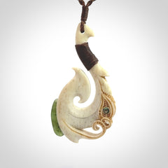 This picture shows a carved manaia matau in bone with Jade and Paua shell. It is provided with a hand-plaited brown cord that is length adjustable. Free shipping worldwide.