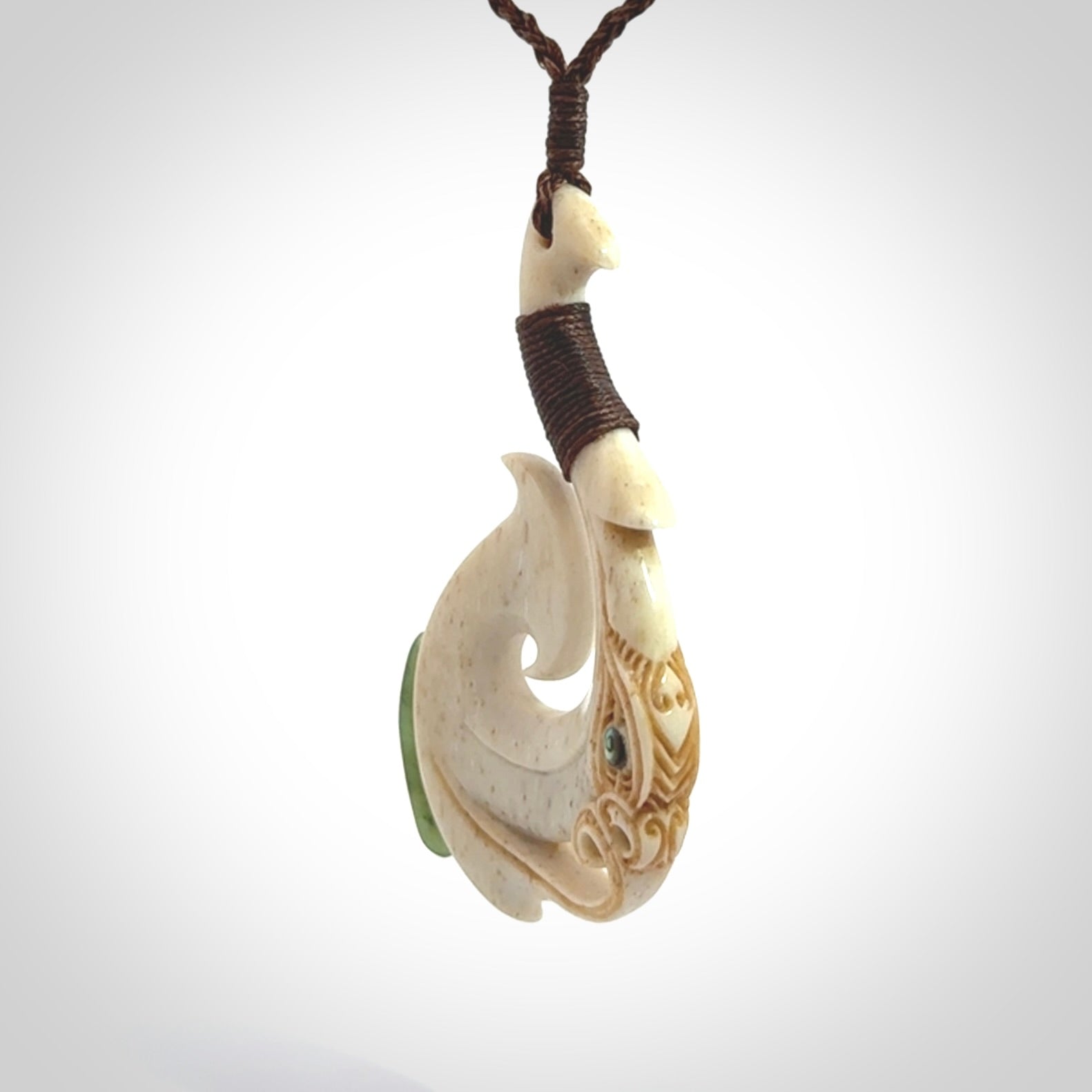 This picture shows a carved manaia matau in bone with Jade and Paua shell. It is provided with a hand-plaited brown cord that is length adjustable. Free shipping worldwide.