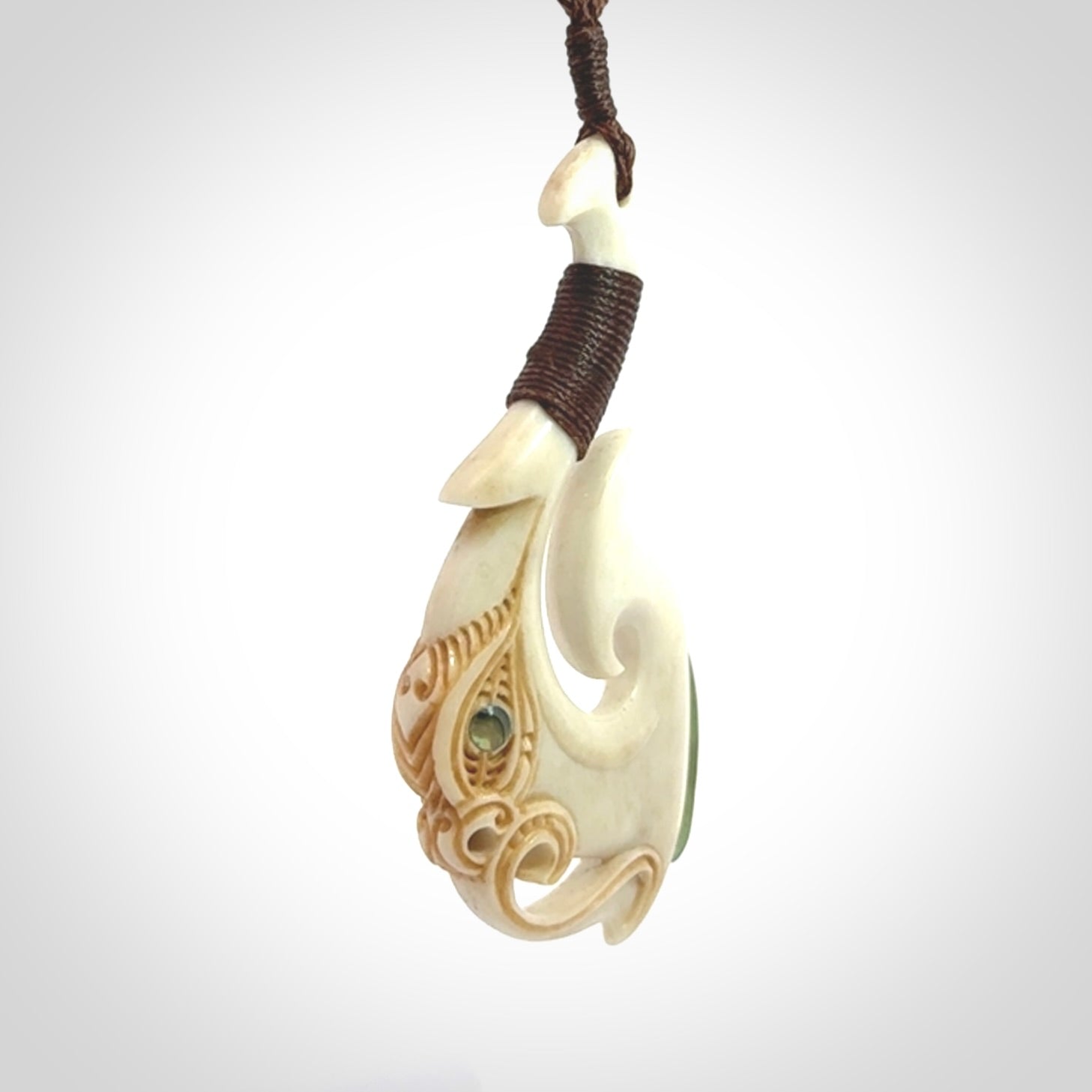 This picture shows a carved manaia matau in bone with Jade and Paua shell. It is provided with a hand-plaited brown cord that is length adjustable. Free shipping worldwide.