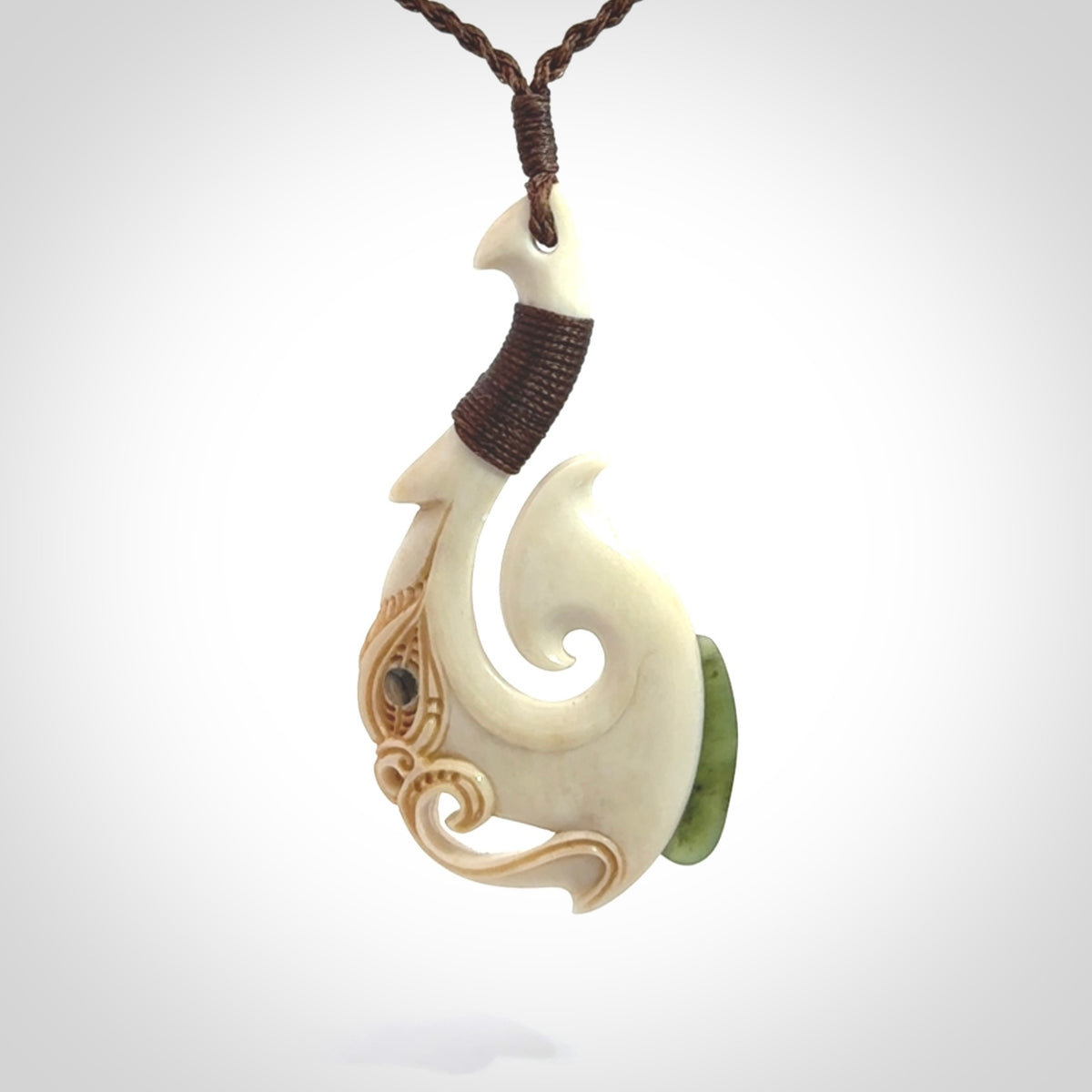 This picture shows a carved manaia matau in bone with Jade and Paua shell. It is provided with a hand-plaited brown cord that is length adjustable. Free shipping worldwide.