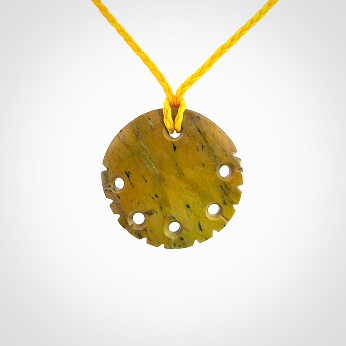 This piece is a smaller sized, oval round, disc pendant. It was carved for us by Alex Sands from a lovely bright and orange piece of New Zealand Flower jade with incredible orange and greens colours at throughout the stone. It is suspended on a yellow coloured braided cord that is length adjustable.