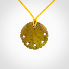This piece is a smaller sized, oval round, disc pendant. It was carved for us by Alex Sands from a lovely bright and orange piece of New Zealand Flower jade with incredible orange and greens colours at throughout the stone. It is suspended on a yellow coloured braided cord that is length adjustable.