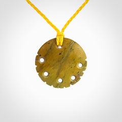 This piece is a smaller sized, oval round, disc pendant. It was carved for us by Alex Sands from a lovely bright and orange piece of New Zealand Flower jade with incredible orange and greens colours at throughout the stone. It is suspended on a yellow coloured braided cord that is length adjustable.
