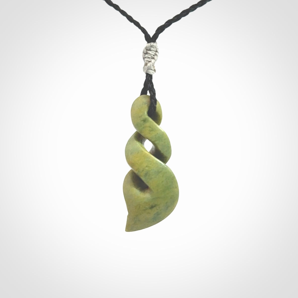 Double twist pendant. Hand carved from rare New Zealand flower jade this is a beautiful pounamu pendant. The cord is hand plaited in a black colour and is length adjustable. It has a floret in silver. It is a delicate and very beautiful greenstone pendant. For sale online by NZ Pacific.