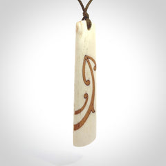 A hand carved, double sided, bone toki with triple koru, intricate pendant. The cord is a marrakesh colour and is adjustable.