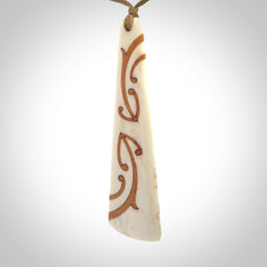 A hand carved, double sided, bone toki with triple koru, intricate pendant. The cord is a camel colour and is adjustable.