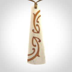 A hand carved, double sided, bone toki with triple koru, intricate pendant. The cord is a camel colour and is adjustable.