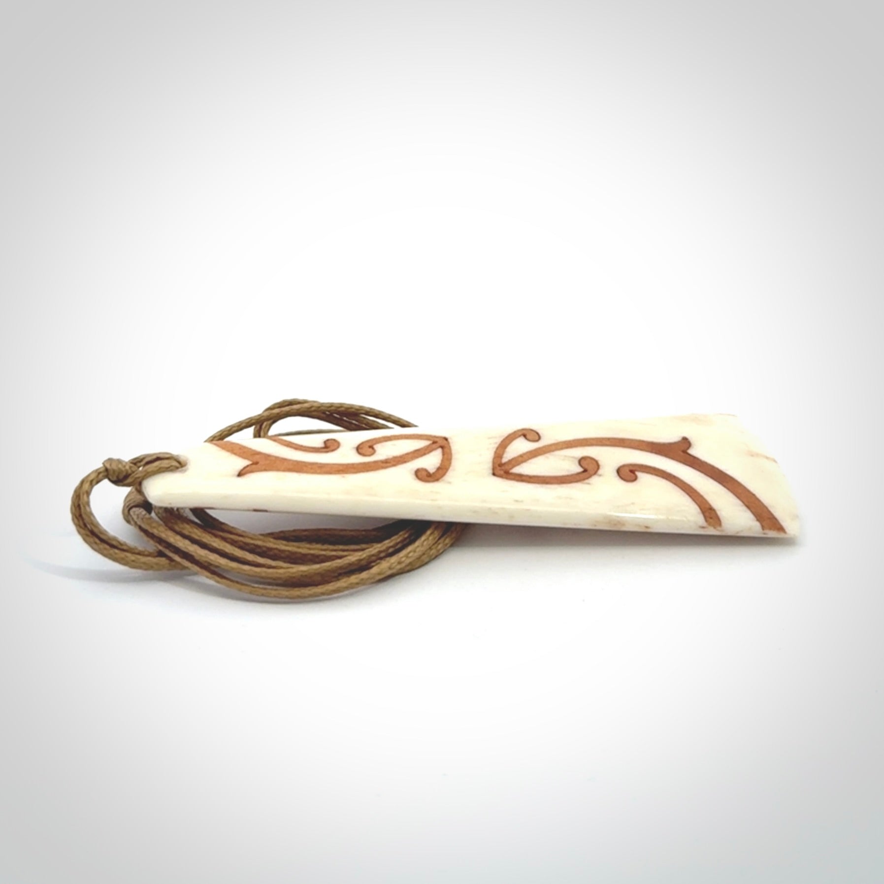 A hand carved, double sided, bone toki with triple koru, intricate pendant. The cord is a camel colour and is adjustable.