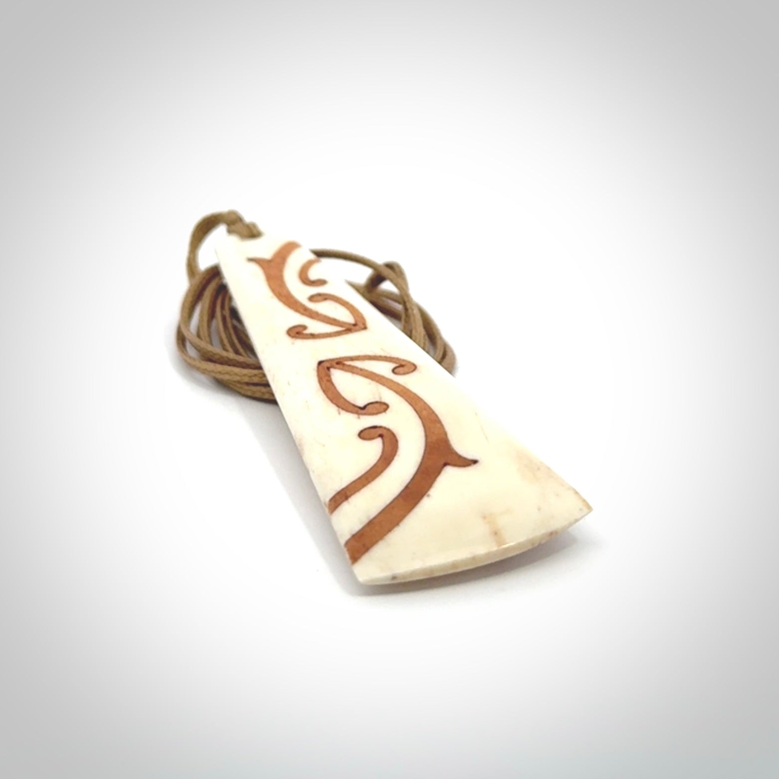 A hand carved, double sided, bone toki with triple koru, intricate pendant. The cord is a camel colour and is adjustable.